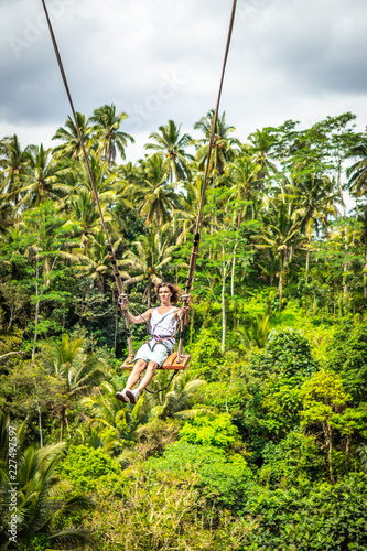 Young tourist man with long hair swinging on the cliff in the jungle rainforest of a tropical Bali island.