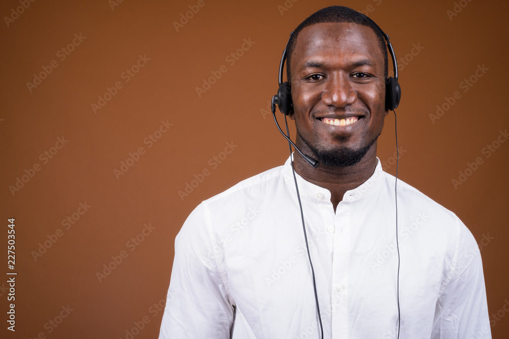 Handsome African businessman wearing headset against brown backg Handsome African businessman wearing headset against brown backg