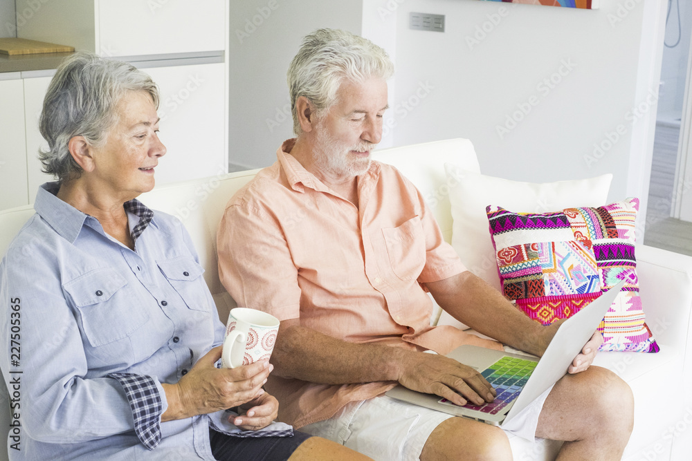Obraz premium senior adult caucasian people couple at home using technology with internet connected laptop with coloured keyboard. together forever lifestyle for man and woman aged with white hair lifestyle