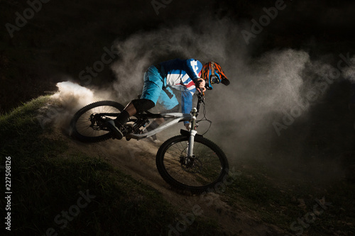 A cyclist on a mountain bike with dusty aggressive turns. Downhill riding at dark night. Bicyclist on a bicycle.