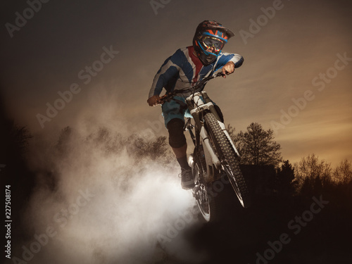 Jump on a mountain bike. Biker making a stunt and jumps in the air. Cool athlete cyclist on a bike flying dust. Downhill biking. MTB