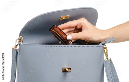 A hand put cosmetic lipsticklip gloss in the female blue gray leather handbag on a white background isolation