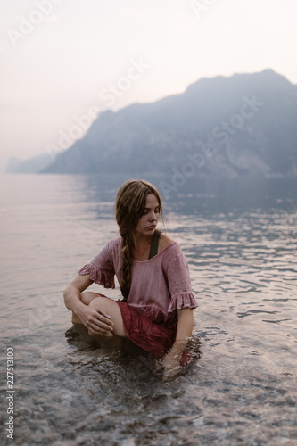 Woman sitting in mountain lake at sunset in italy