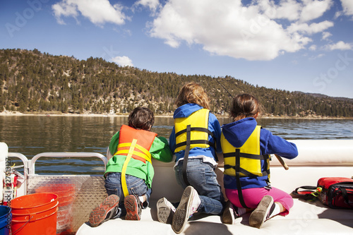 Rear view of children in life vests fishing from yacht