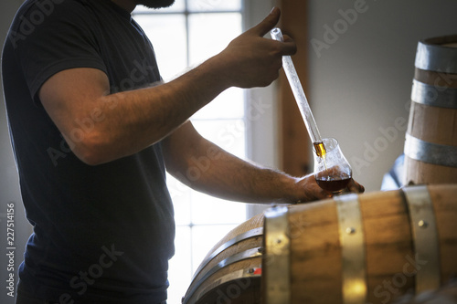 Bild auf Leinwand Midsection of man collecting whiskey from barrel in wineglass
