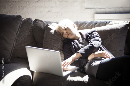 Bored young woman using laptop on sofa at home