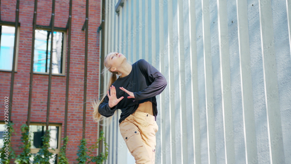 A young girl performs modern hip hop dance on the streets of the city during the summer, twisting and rotating.