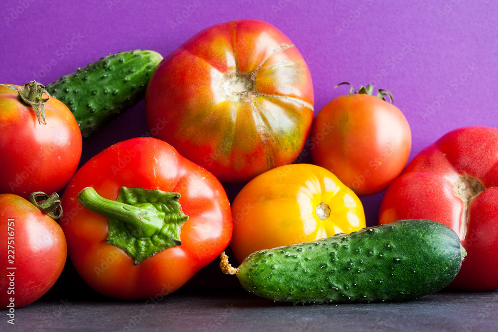 Organic vegetables harvest on purple black background. Ripe bell pepper, yellow red tomatoes cucumbers. Close-up photo