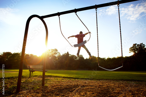 Fotografija Boy jumping from swing at park during sunset