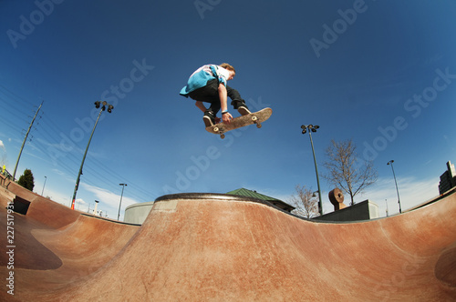 Low angle view of man jumping with skateboard at skate ramp against blue sky