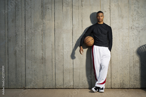 фотографія Portrait of sportsman with basketball standing against wooden wall