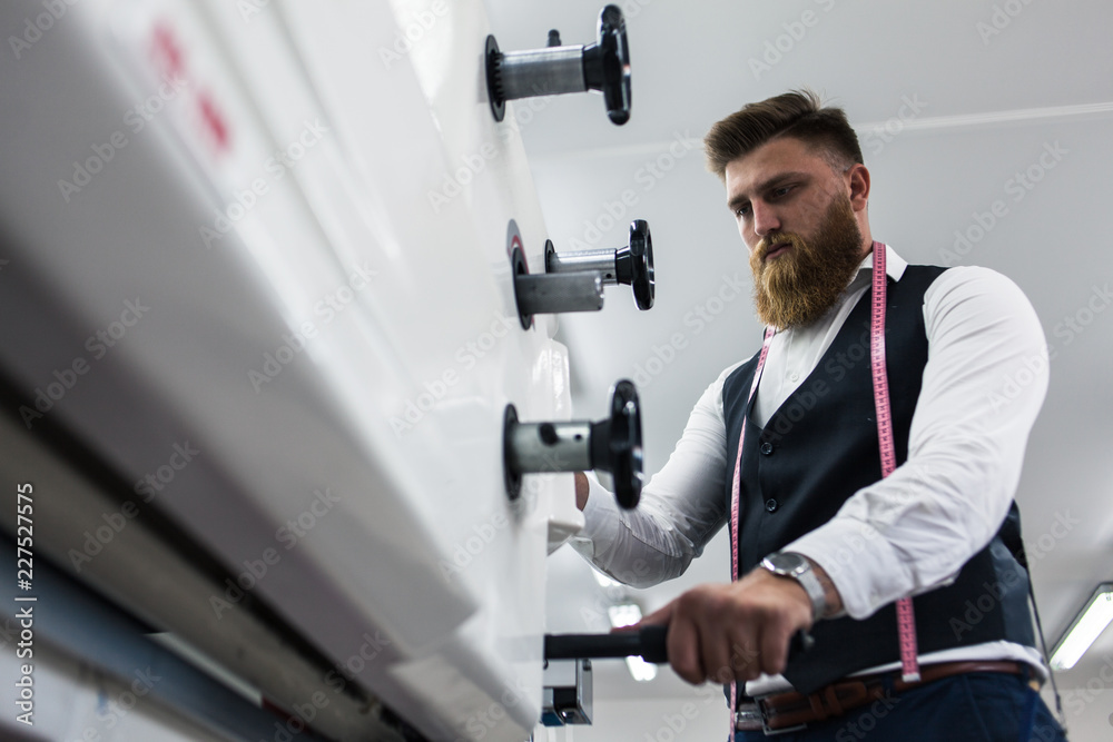 Young bearded man tailor working on new clothing