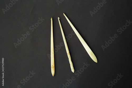 Three old ancient hand carved bone croched hooks needles against black background.