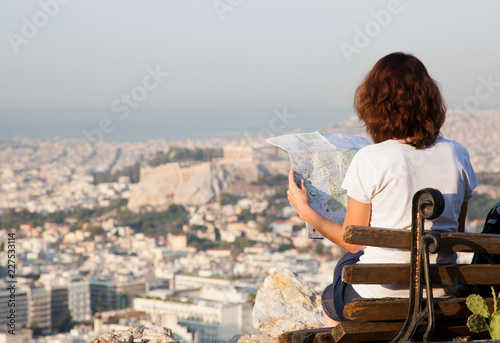 Fototapeta Naklejka Na Ścianę i Meble -  woman with a map sitting on Lycabettus Hill, the highest point in the city overlooking Athens with the Acropolis - world traveller