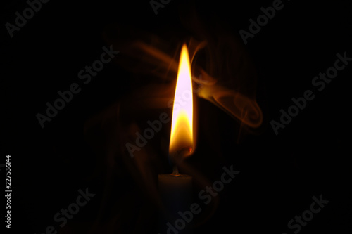 Glowing Orange and White Candle Flame With Swirling Wisps of Smoke Centered Against a Black Background