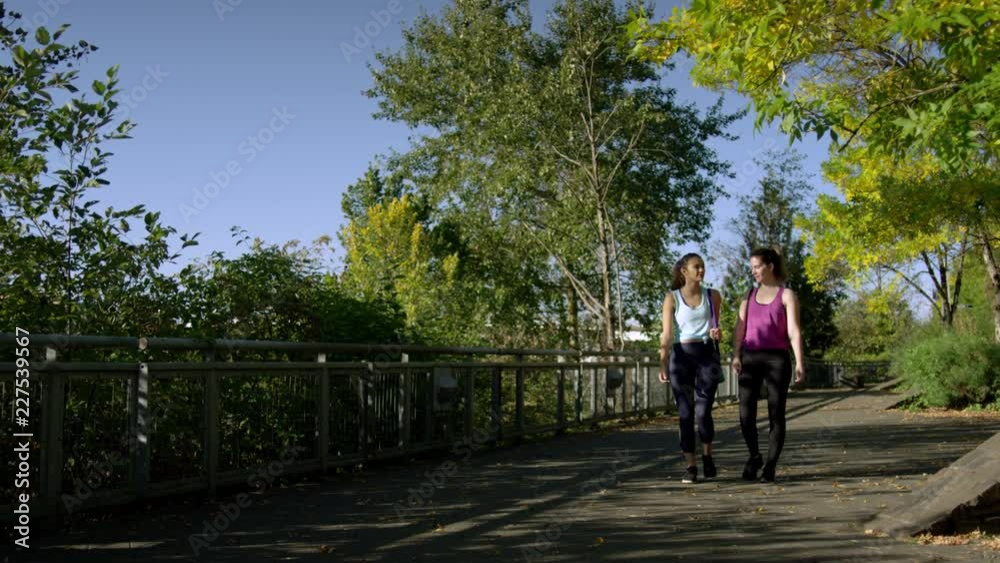 Happy Young Women Walk Through Park On Sunny Autumn Day, Carrying Yoga Mats, Slow Motion Happy Young Women Walk Through Park On Sunny Autumn Day, Carrying Yoga Mats, Slow Motion