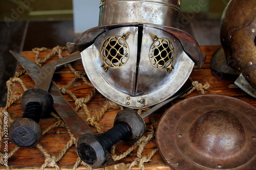 Roman gladiator helmet, as worn by Gallus or Murmillo gladiators, displayed with a selection of swords, and a small shield