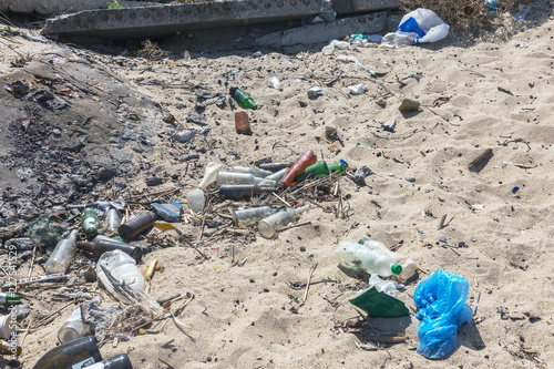 Spilled garbage on beach of big city. Empty used dirty plastic bottles. Dirty sea sandy shore Black Sea. Environmental pollution. Ecological problem. Garbage dump near fence of public beach