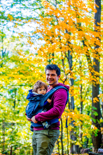 Young father with a child in carrier. located in autumn season park