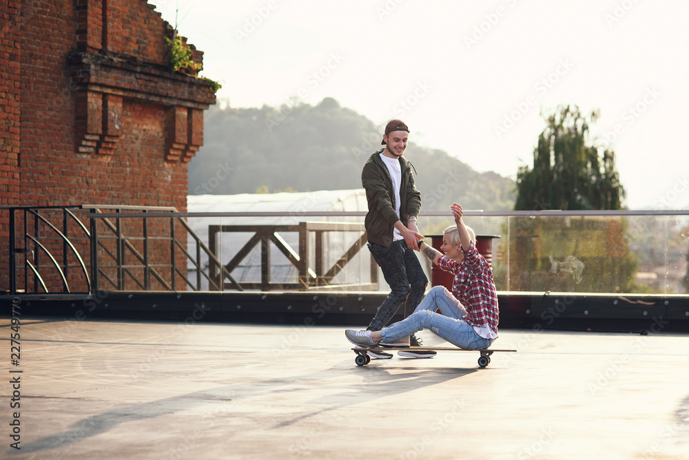 Handsome young couple having fun with skateboards on the roof of industrial building. Modern urban active lifestyle concept.