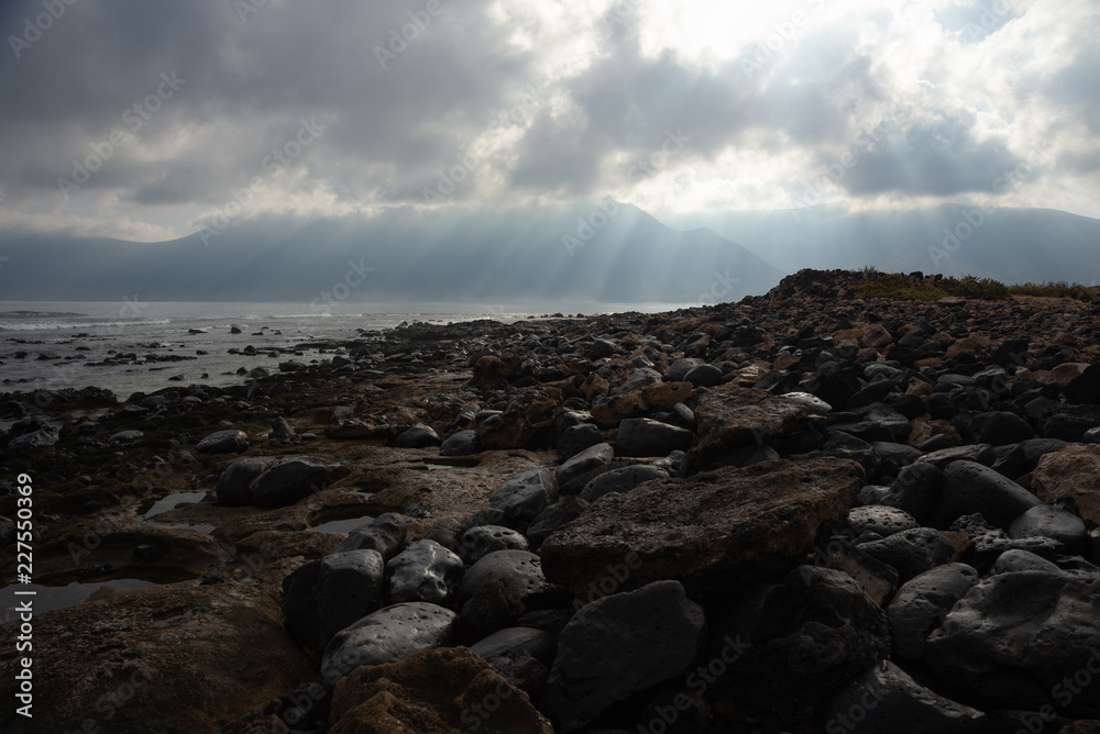 the sun's rays against the backdrop of the mountains and the lava-rocky wet shore in the foreground the sun's rays against the backdrop of the mountains and the lava-rocky wet shore in the foreground