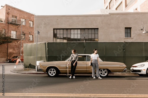 Two young stylish women standing together in front of vintage car photo