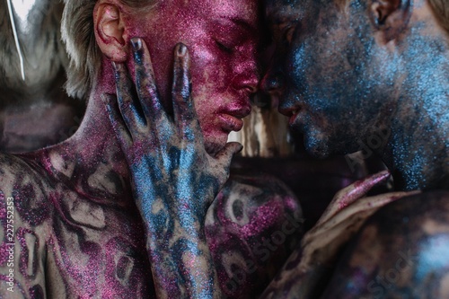 Closeup portrait of couple of girls with bright pink and blue shiny bodyart embracing each other with closed eyes
