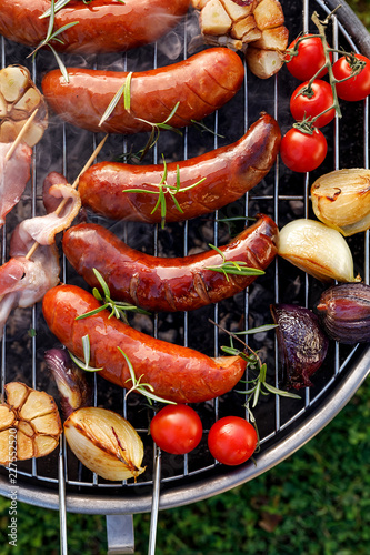 Grilled food. Grilled pork sausage, bacon and vegetables on the grill plate, top view, outdoor. Barbecue, bbq