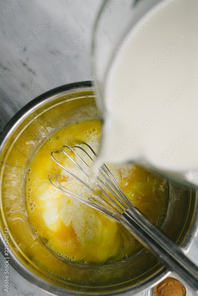 Pouring milk into whisked eggs for a recipe Pouring milk into whisked eggs for a recipe