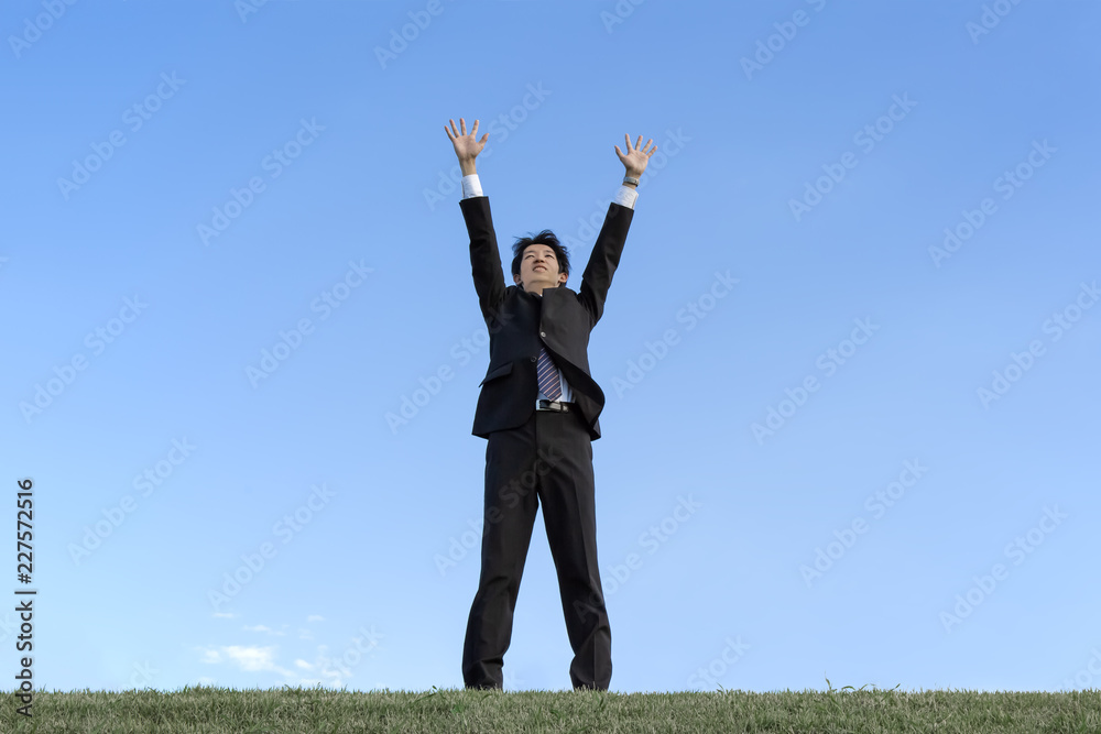 青空をバックに空に向かい手を広げる若い男性1人。成功・勝者・パワー・挑戦イメージ