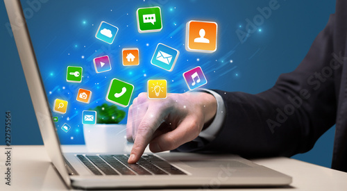Businessman hand typing on laptop with flying application icons around
