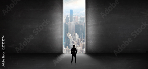Businessman standing in a dark room and looking outside to a cityscape view
