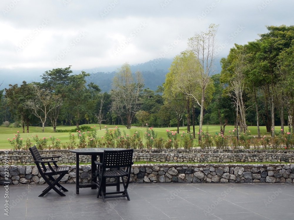 Patio table and chairs with a view across a golf course to forest and mountains in the Khao Soi Dow district of eastern Thailand.