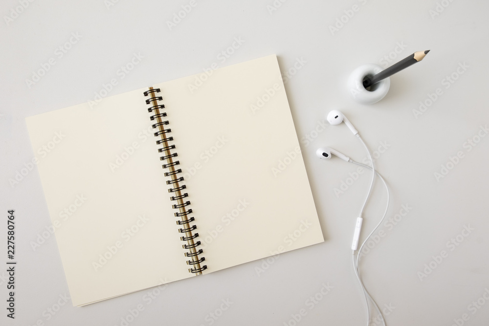 Top view open blank notebook, earphone, and pencil in holder on white desk background Top view open blank notebook, earphone, and pencil in holder on white desk background