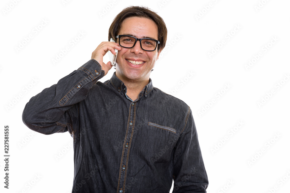 Studio shot of young happy Persian man smiling while talking on Studio shot of young happy Persian man smiling while talking on