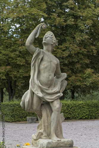 A stone figure of a half-naked man in a park.