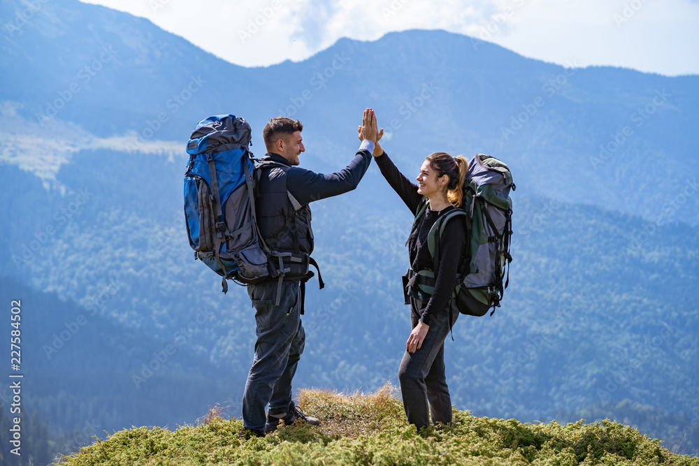 The happy couple with backpacks standing on the mountain landscape background The happy couple with backpacks standing on the mountain landscape background