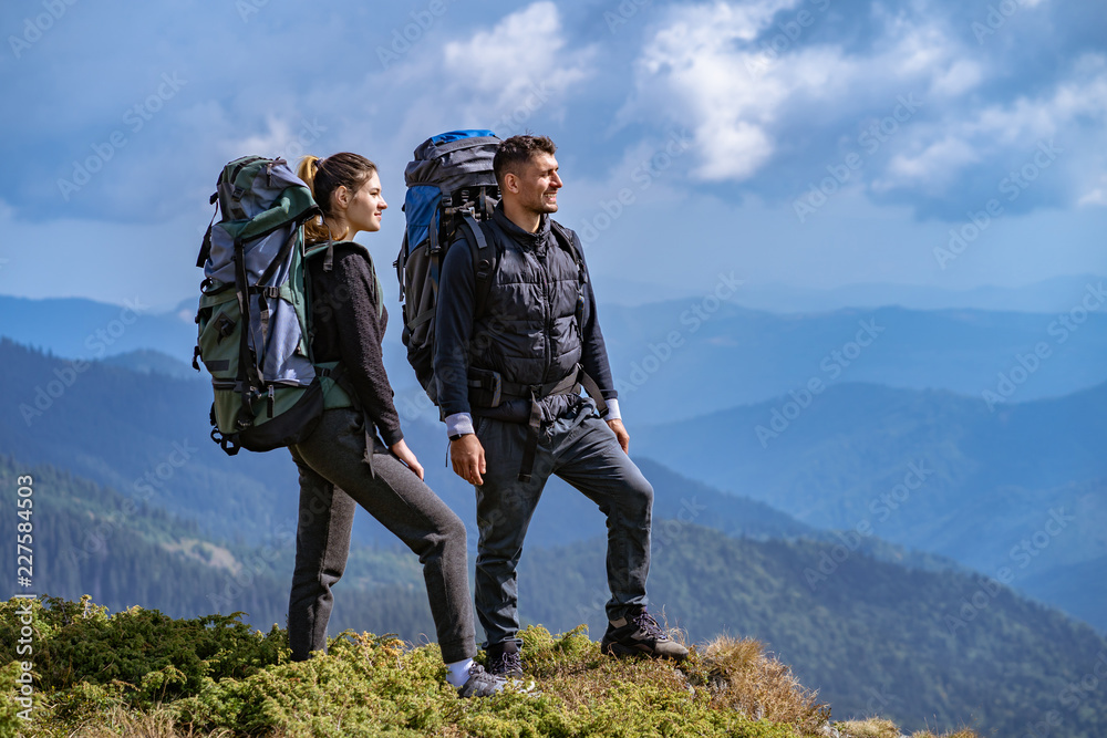 The couple with backpacks enjoying on a beautiful mountain landscape background