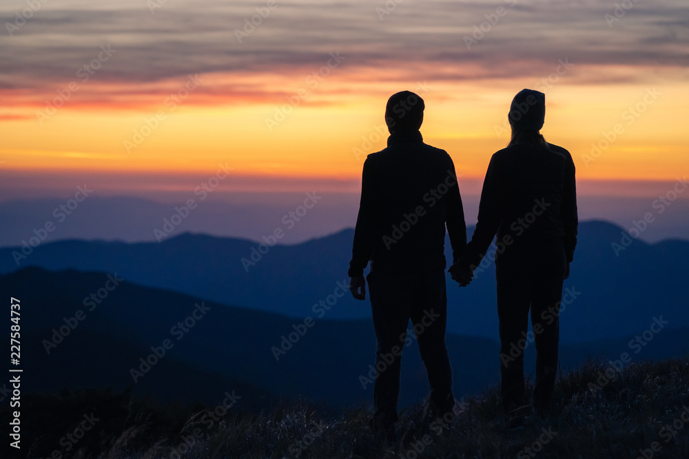 The silhouette of the couple on the mountain with a sunset background