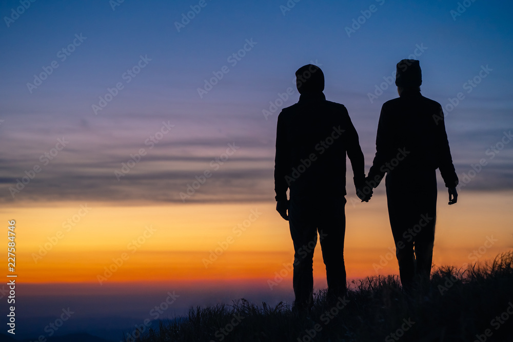 The silhouette of the couple on the mountain with a sunrise background