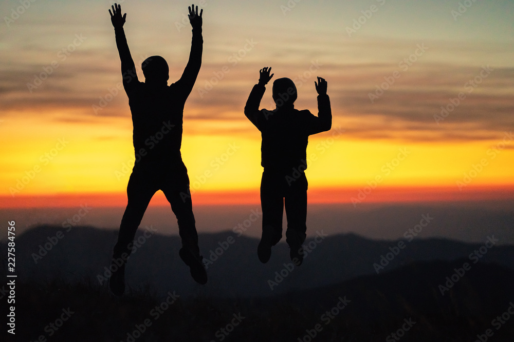 The man and a woman jumping on the mountain on the sunset background