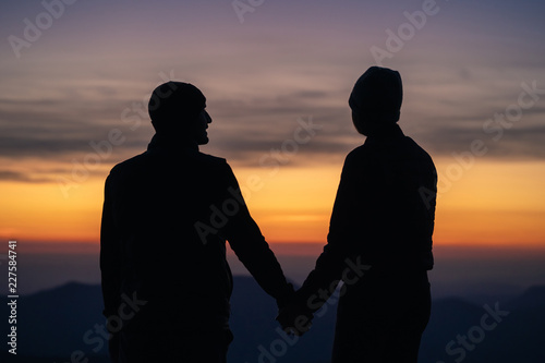 The silhouette of the couple on the mountain with a sunrise background