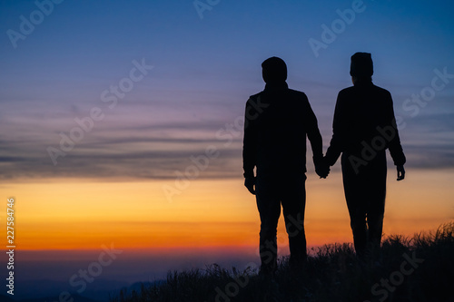 The silhouette of the couple on the mountain with a sunrise background © realstock1