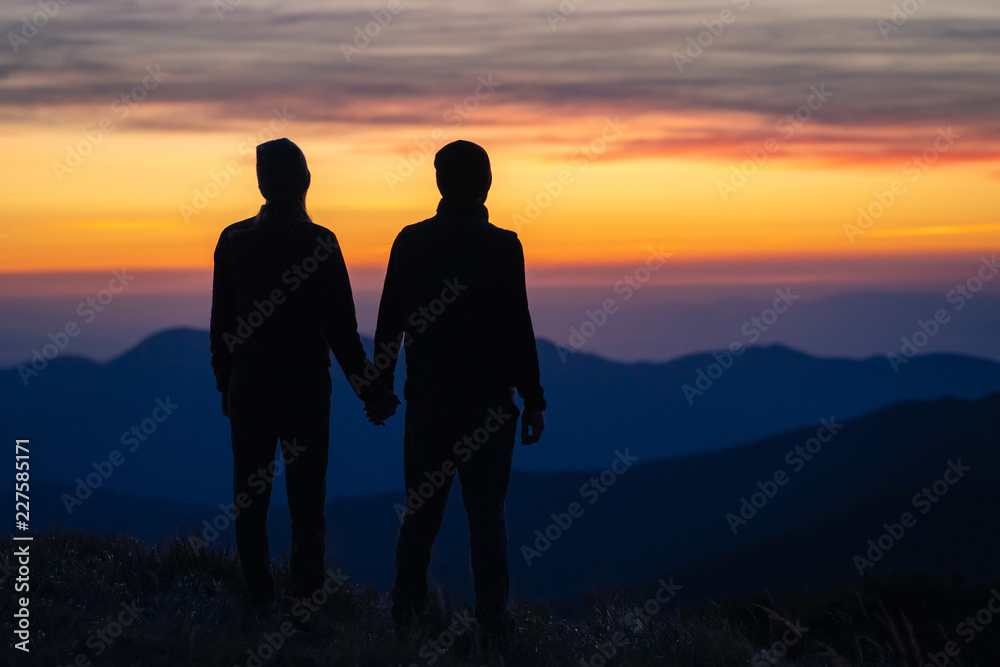The silhouette of the couple on the mountain with a sunset background The silhouette of the couple on the mountain with a sunset background