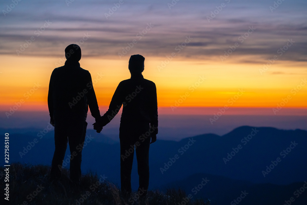 The couple standing on the mountain on a sunrise background