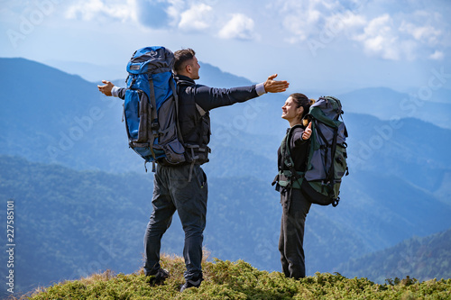 The happy couple with backpacks standing on the mountain landscape background