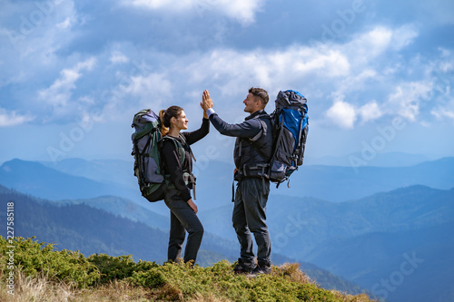 The happy couple with backpacks gesturing on the mountain