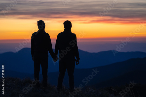 The silhouette of the couple on the mountain with a sunset background