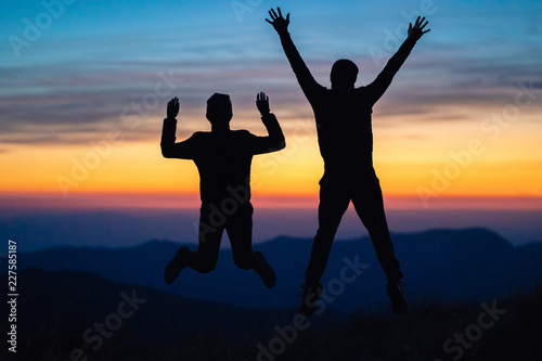 The man and a woman jumping on the mountain on the sunset background