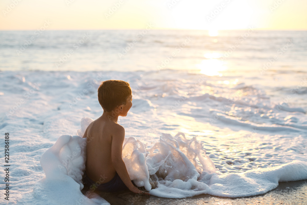 Happy little boy enjoying ocean water at sunset Happy little boy enjoying ocean water at sunset